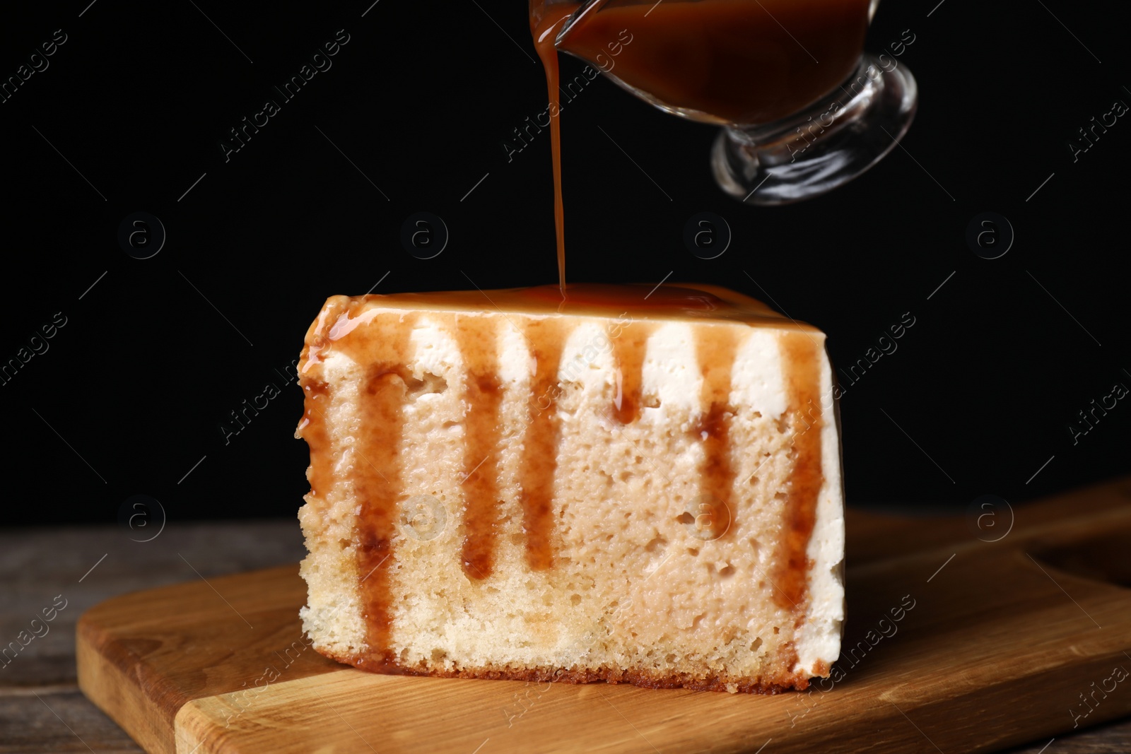 Photo of Pouring caramel sauce on slice of cake at wooden table