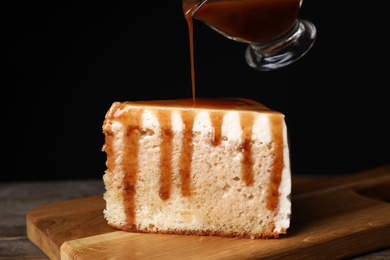 Pouring caramel sauce on slice of cake at wooden table