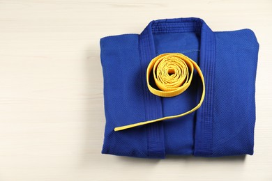 Photo of Yellow karate belt and blue kimono on wooden background, top view. Space for text