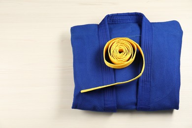 Yellow karate belt and blue kimono on wooden background, top view. Space for text