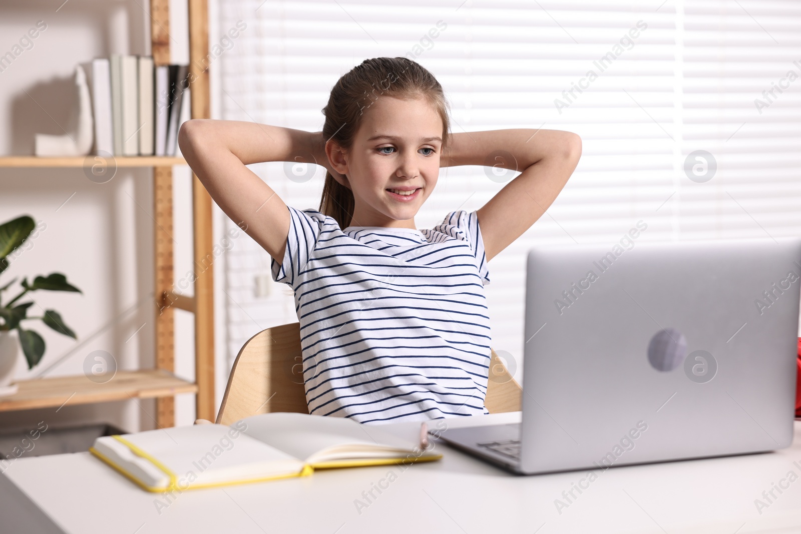 Photo of E-learning. Cute girl using laptop during online lesson at table indoors