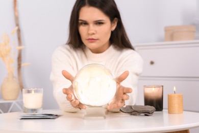 Photo of Soothsayer predicting future at table in room, focus on crystal ball