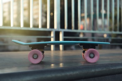 Photo of Modern light blue skateboard with pink wheels on top of ramp outdoors