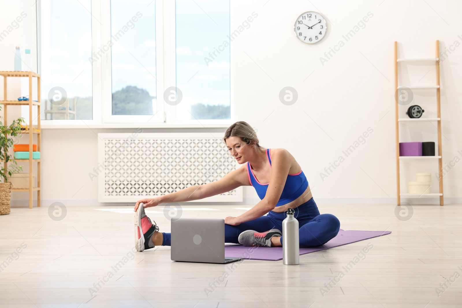 Photo of Online fitness trainer. Woman doing exercise near laptop at home