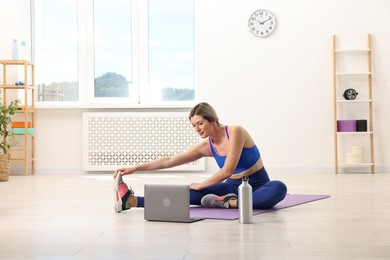 Online fitness trainer. Woman doing exercise near laptop at home