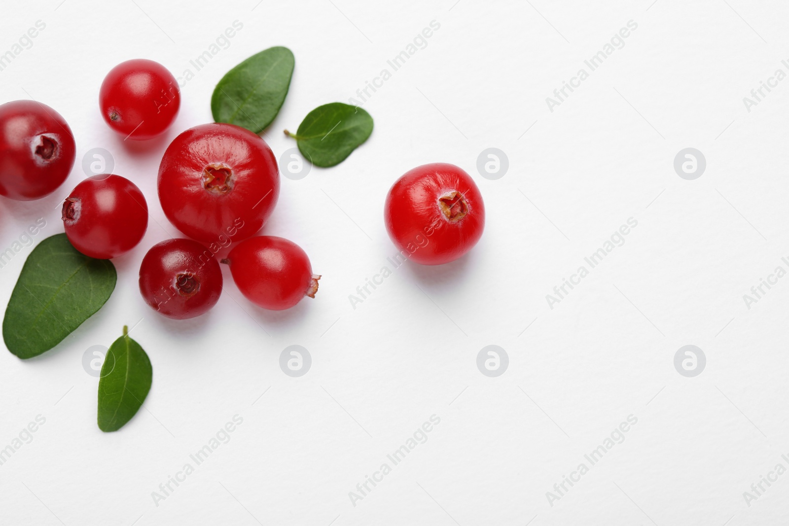 Photo of Fresh ripe cranberries and green leaves on white background, flat lay. Space for text