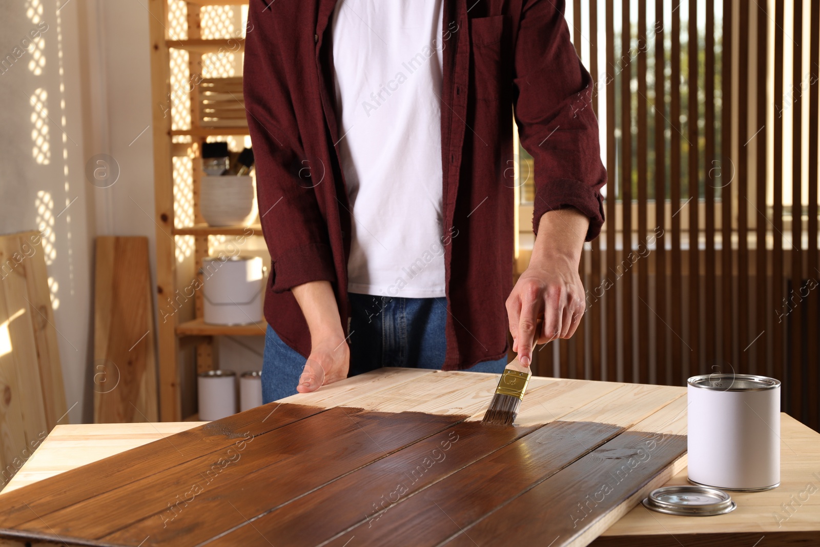 Photo of Man with brush applying wood stain onto wooden surface indoors, closeup