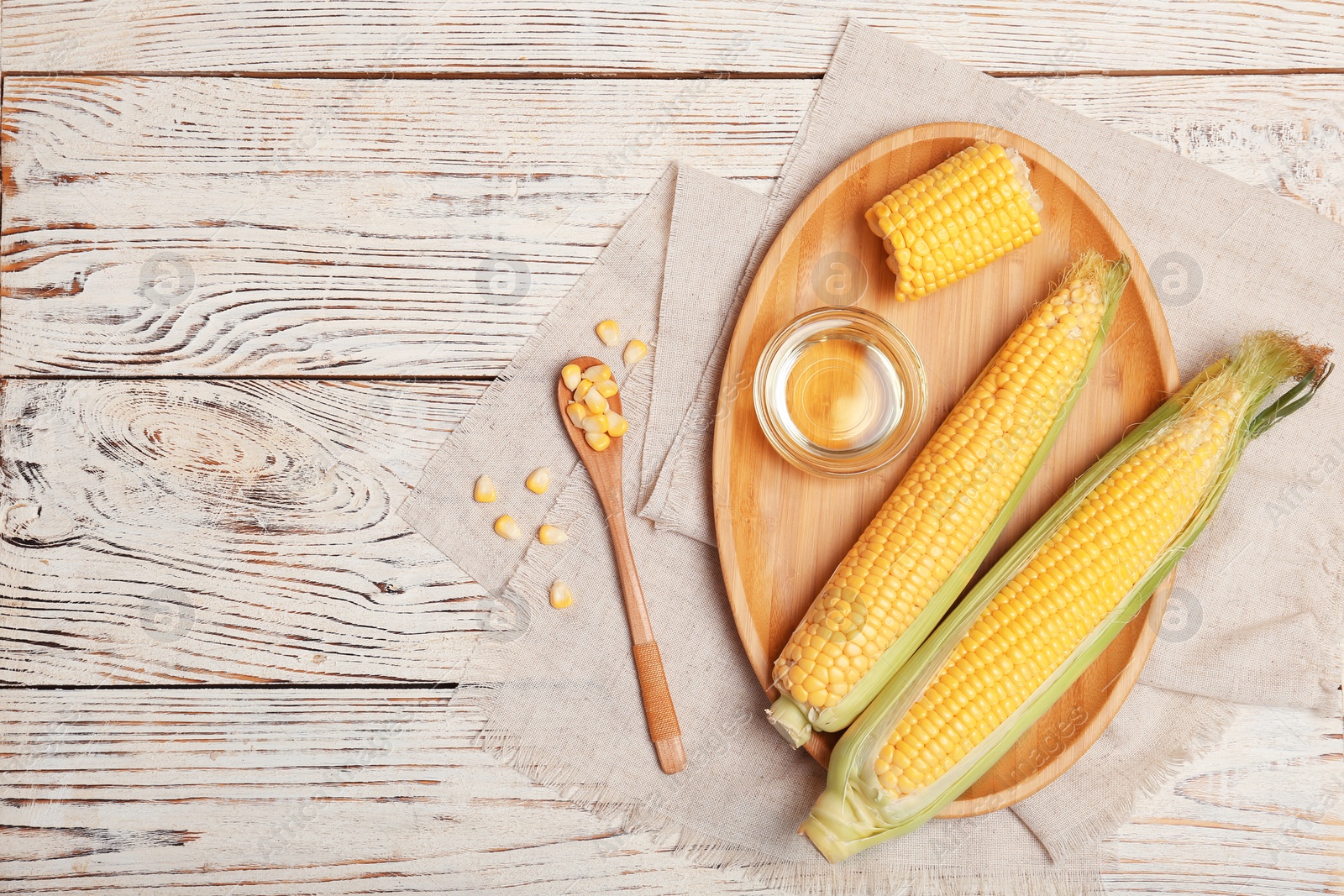 Photo of Flat lay composition with corn cobs and bowl of oil on wooden background