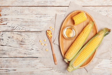 Photo of Flat lay composition with corn cobs and bowl of oil on wooden background