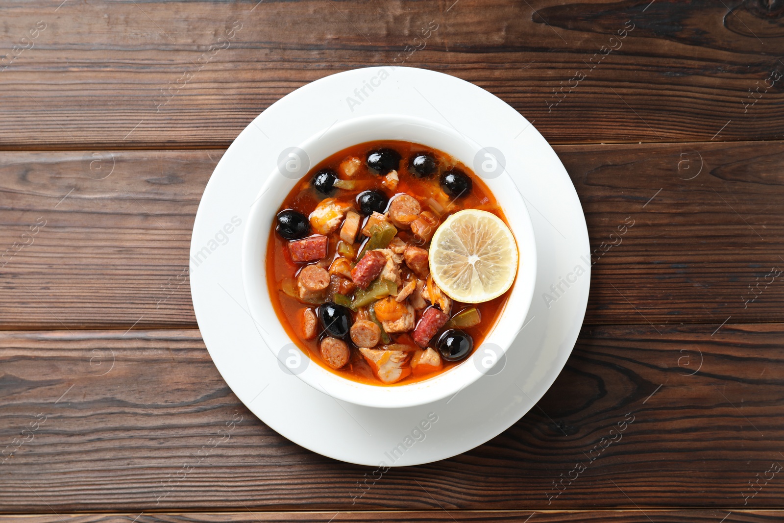 Photo of Meat solyanka soup with sausages, olives and vegetables on wooden table, top view