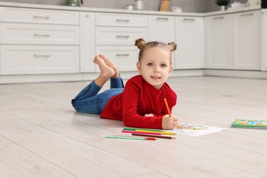 Cute little girl coloring on warm floor in kitchen. Heating system