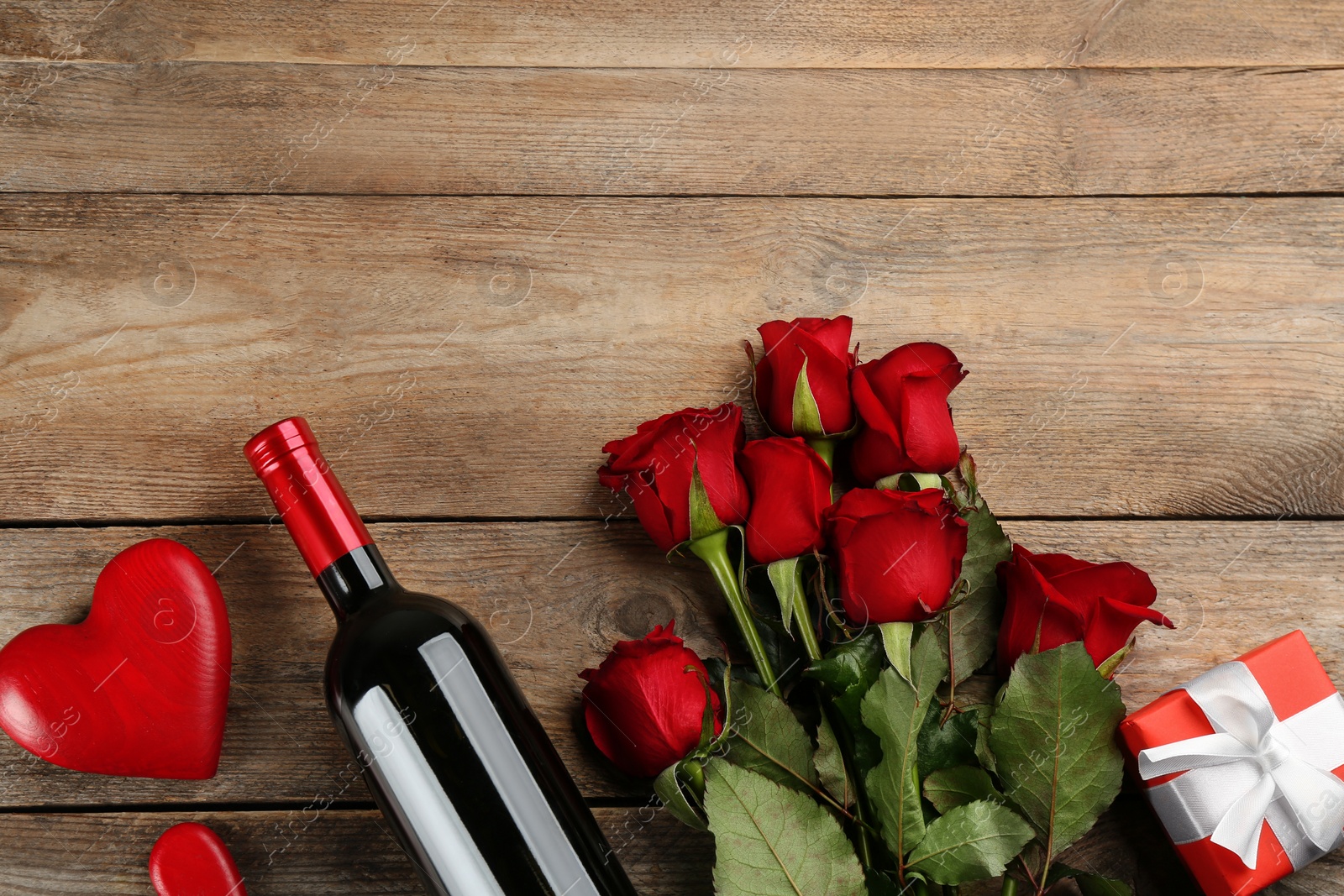 Photo of Flat lay composition with beautiful red roses and bottle of wine on wooden background, space for text. Valentine's Day celebration
