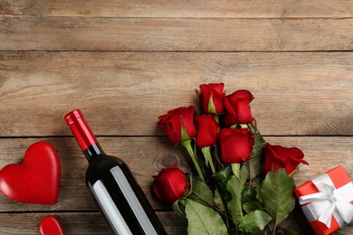 Flat lay composition with beautiful red roses and bottle of wine on wooden background, space for text. Valentine's Day celebration