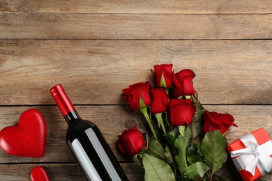 Photo of Flat lay composition with beautiful red roses and bottle of wine on wooden background, space for text. Valentine's Day celebration