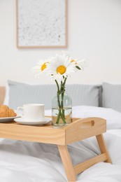 Photo of Bouquet of beautiful daisy flowers and breakfast on wooden tray in bedroom