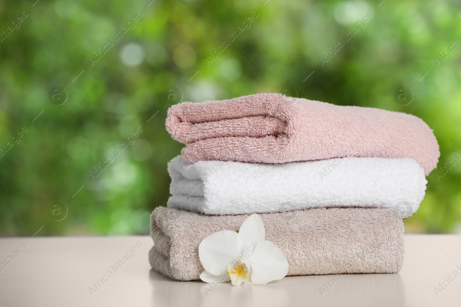 Photo of Stacked towels with flower on white table against blurred background, space for text