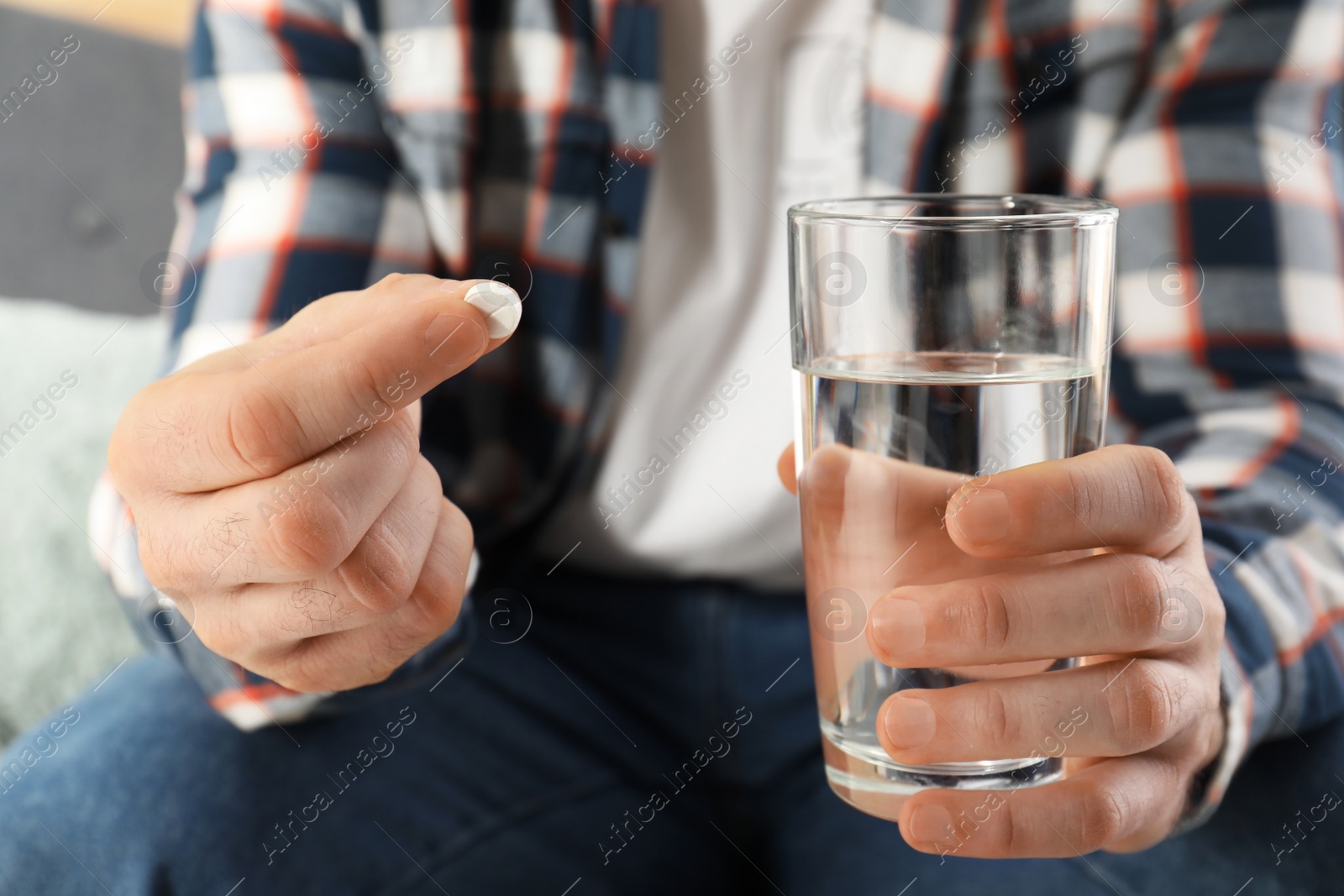 Photo of Man holding pill and glass of water indoors, closeup