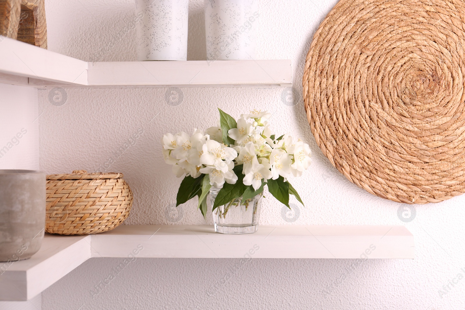 Photo of Beautiful jasmine flowers in vase and decor on shelves indoors