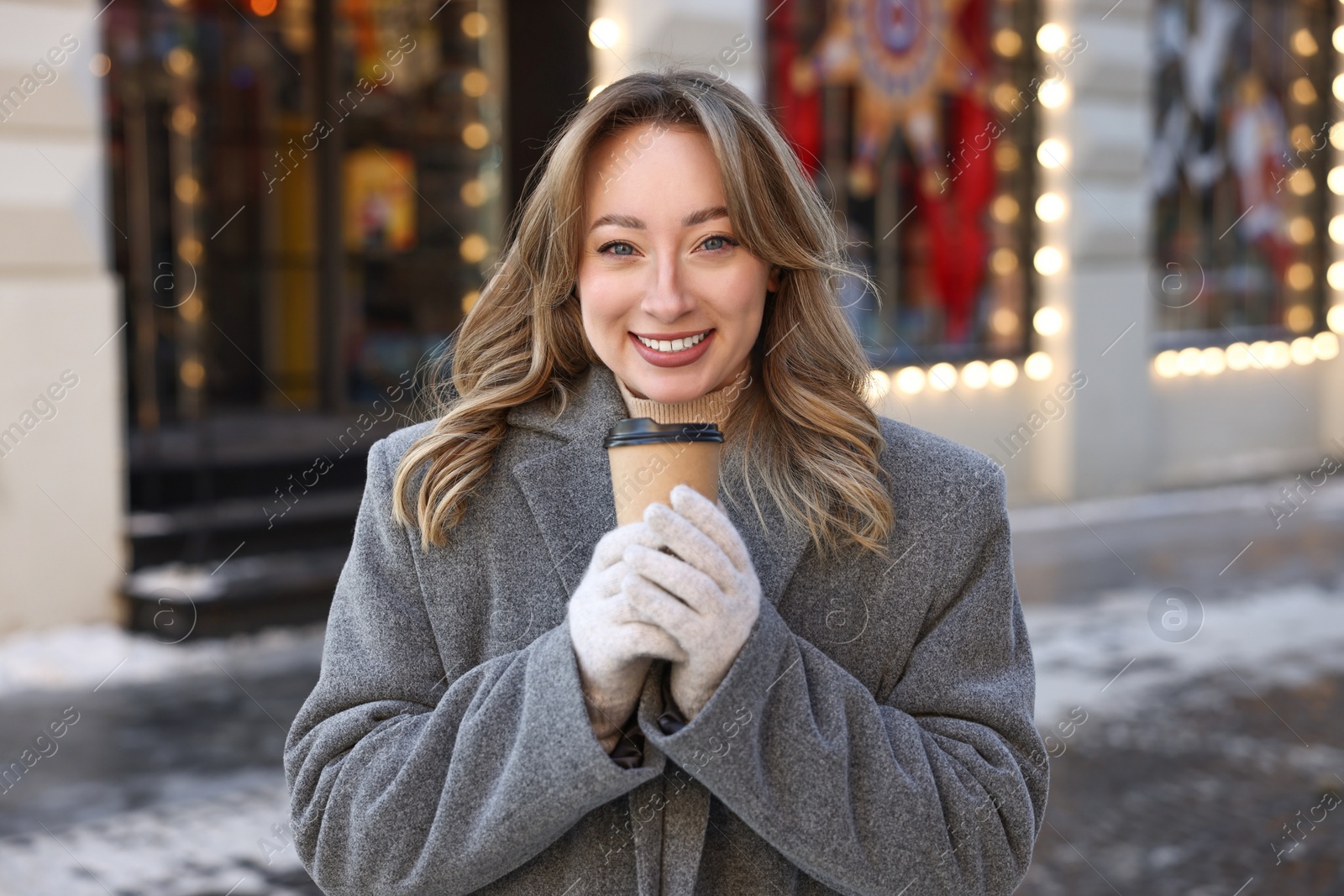 Photo of Portrait of smiling woman with paper cup of coffee on city street in winter