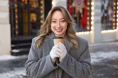 Portrait of smiling woman with paper cup of coffee on city street in winter