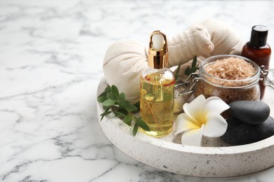 Beautiful spa composition with essential oil and plumeria flower on white marble table, space for text