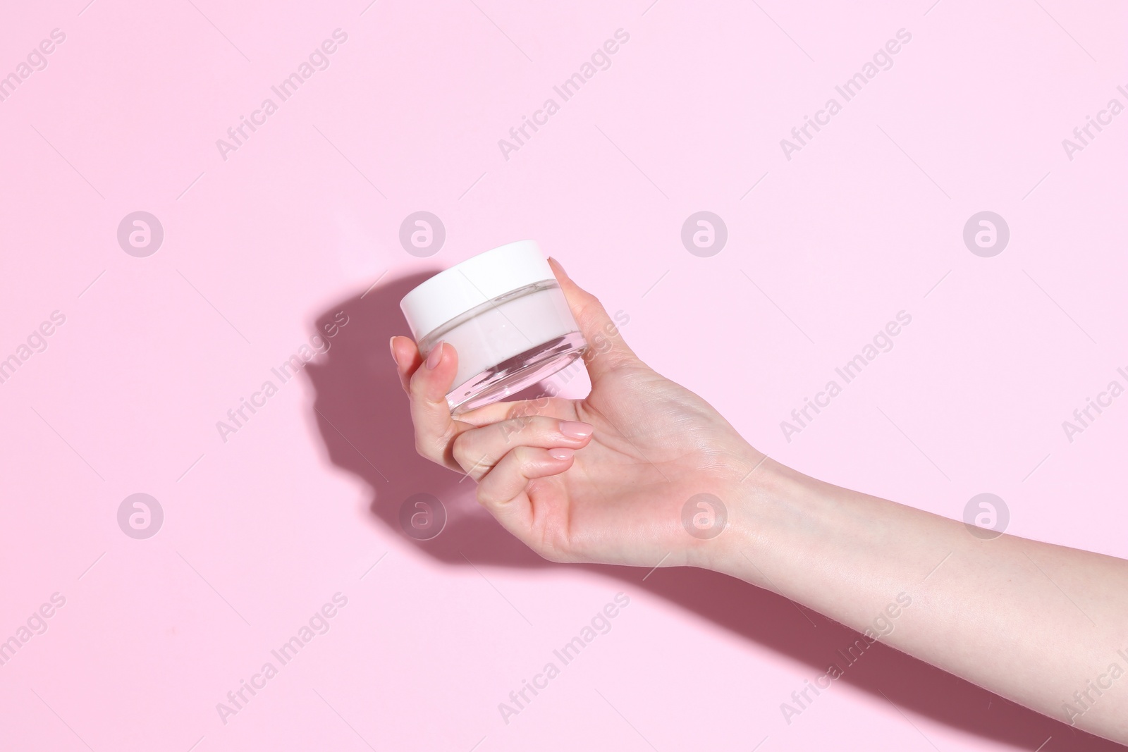 Photo of Woman holding jar of cream on pink background, closeup