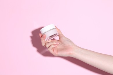 Photo of Woman holding jar of cream on pink background, closeup