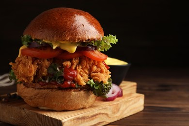 Photo of Delicious burger with crispy chicken patty on wooden table, closeup. Space for text