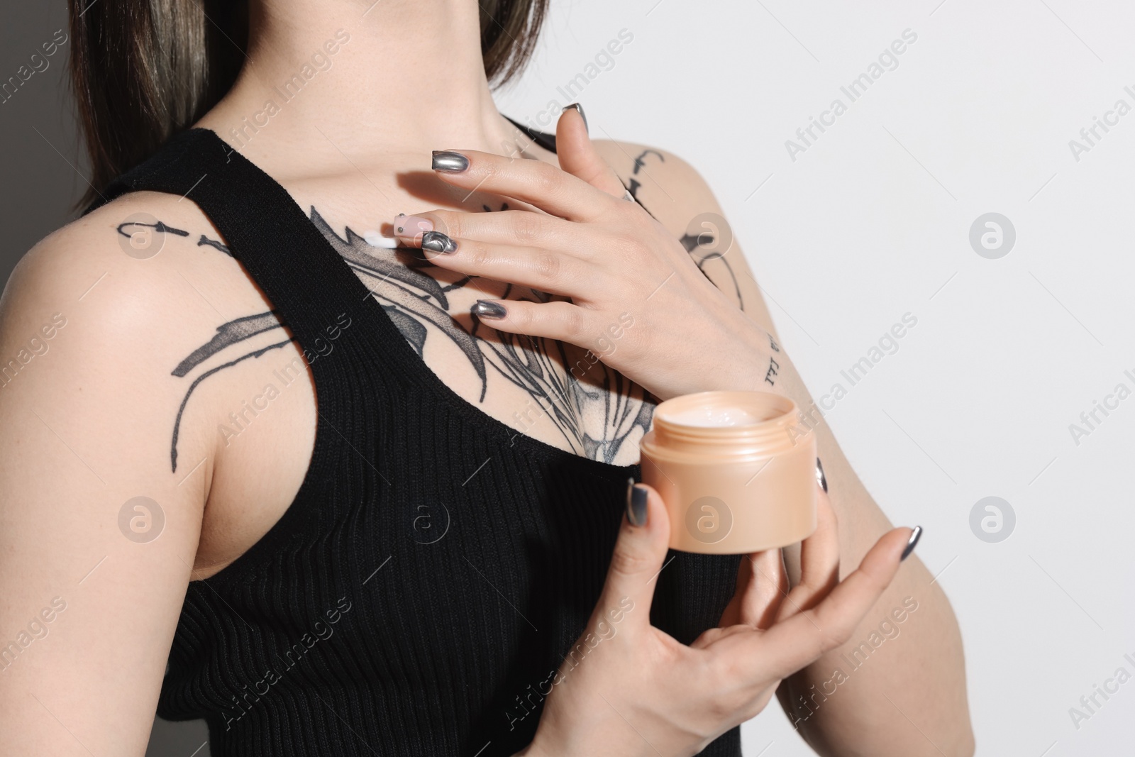 Photo of Woman applying healing cream onto her tattoos against light background, closeup