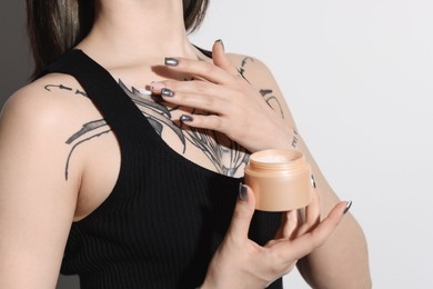 Woman applying healing cream onto her tattoos against light background, closeup