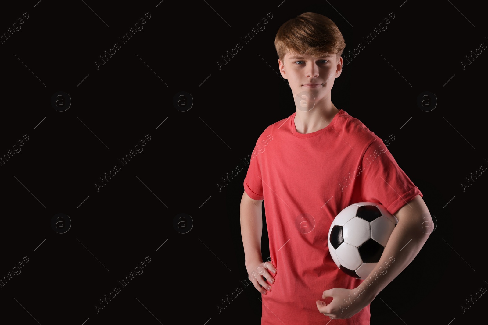 Photo of Teenage boy with soccer ball on black background. Space for text