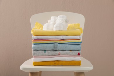 Photo of Stack of baby clothes and booties on chair near beige wall