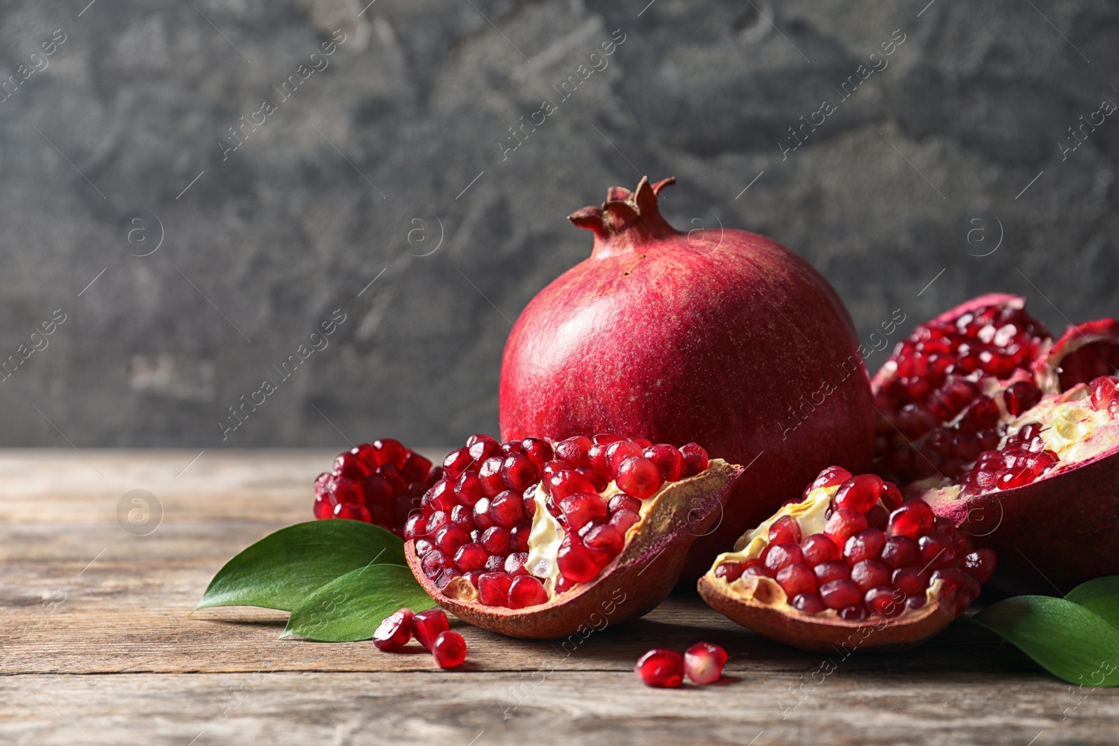 Photo of Ripe pomegranates and leaves on table against grey background. Space for text