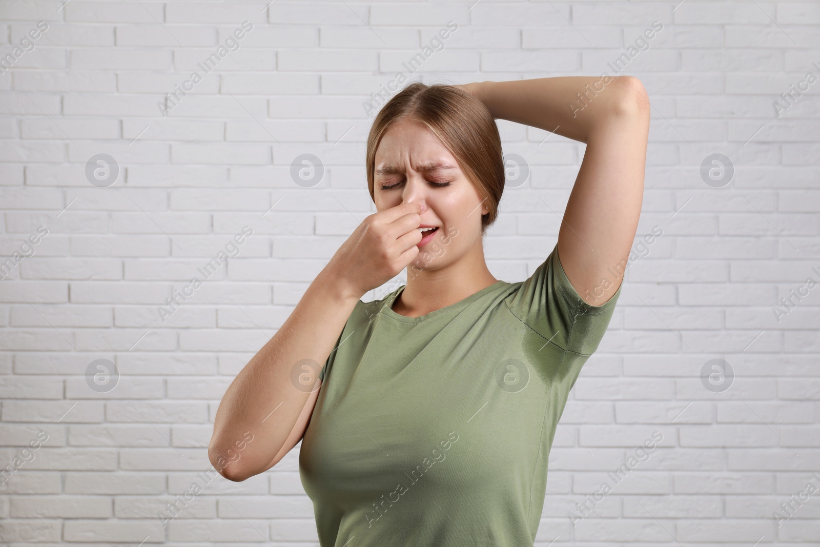 Photo of Young woman with sweat stain on her clothes against brick wall. Using deodorant