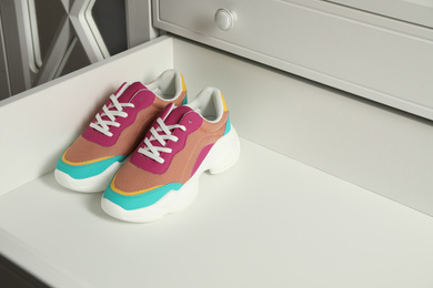 Photo of Colorful sneakers in empty drawer. Footwear storage