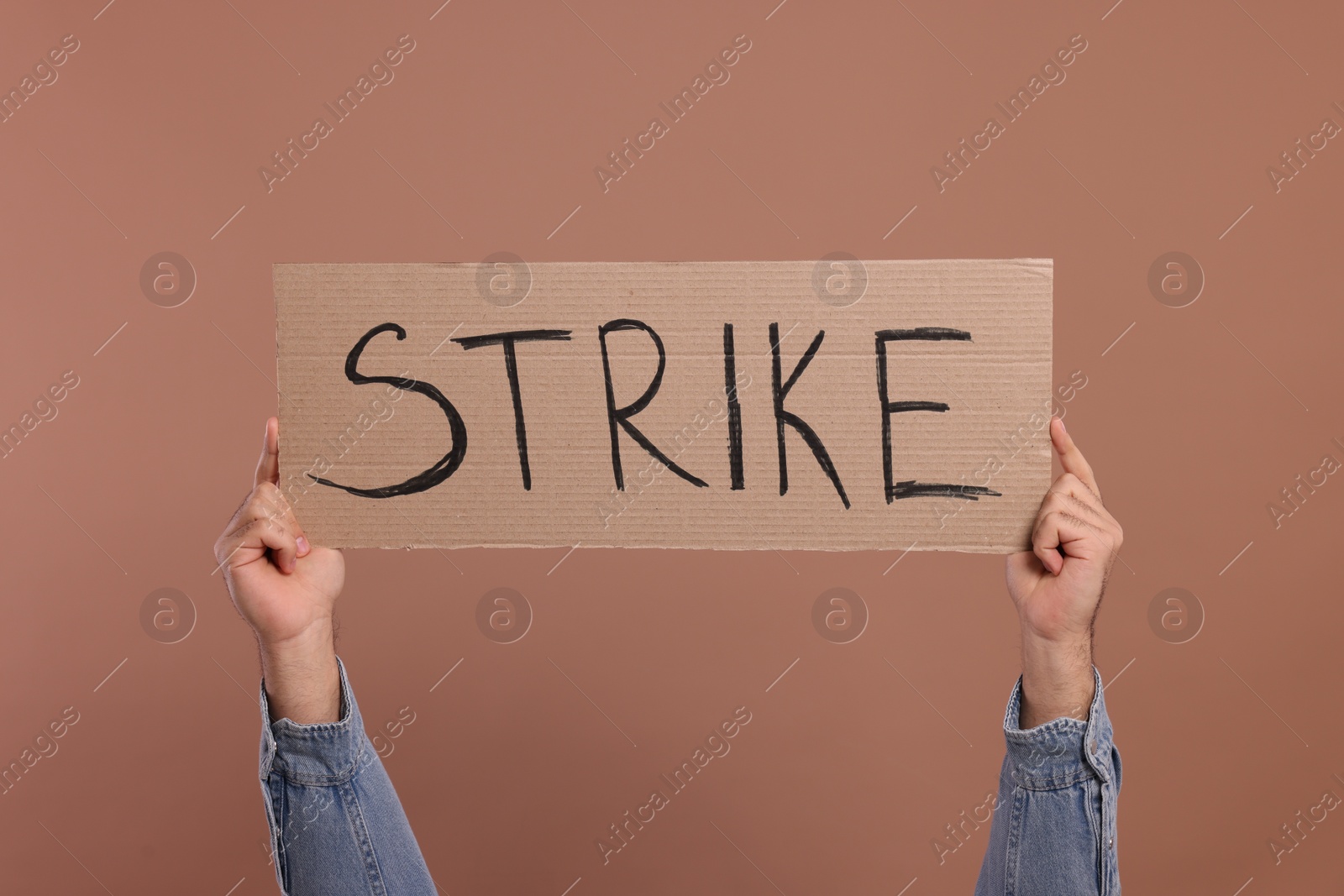 Photo of Man holding cardboard banner with word Strike on brown background, closeup