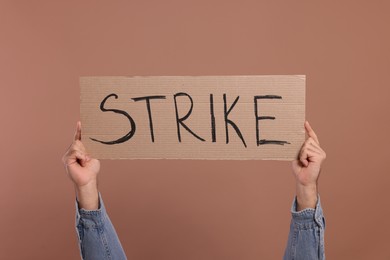 Photo of Man holding cardboard banner with word Strike on brown background, closeup