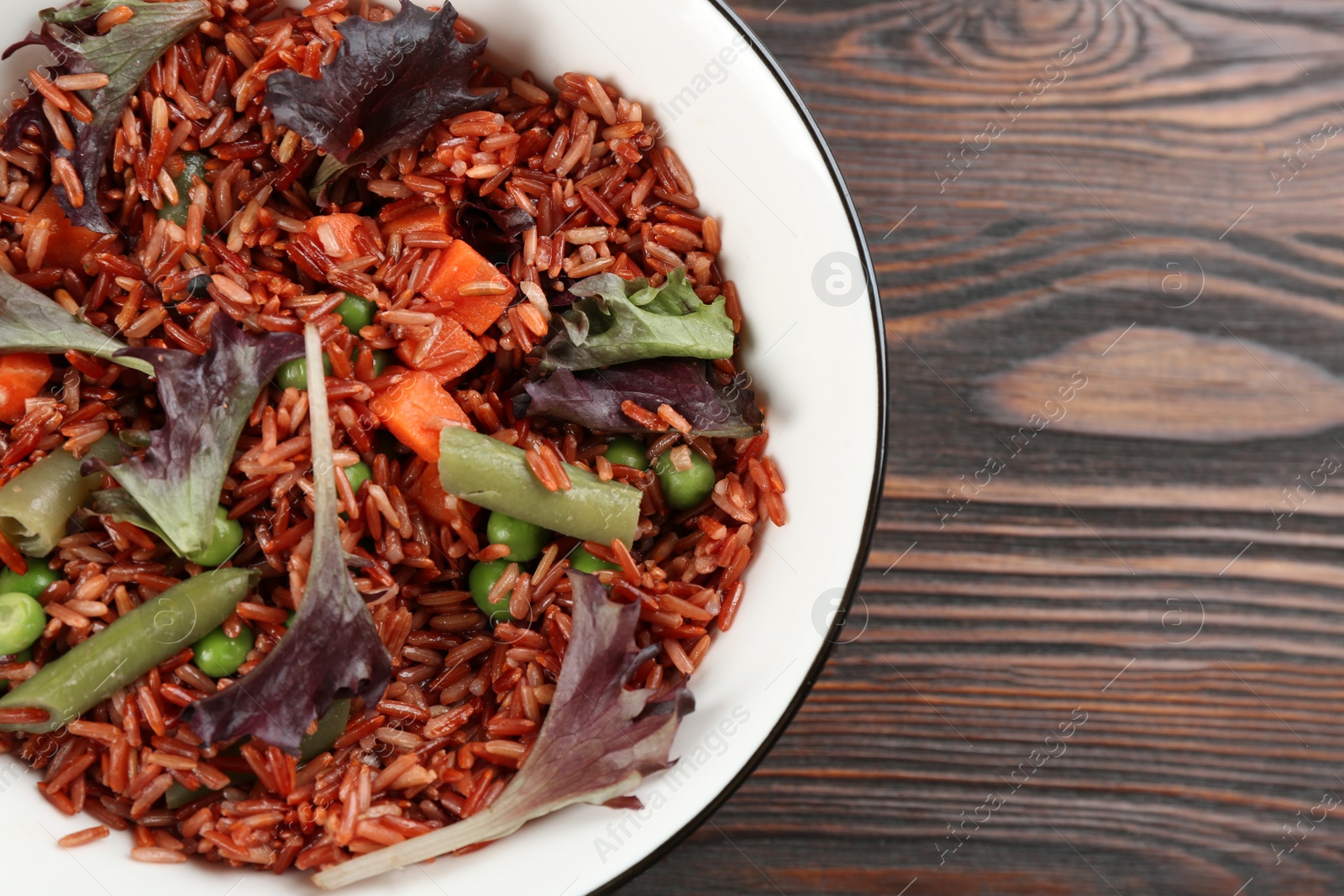 Photo of Tasty brown rice with vegetables on wooden table, top view