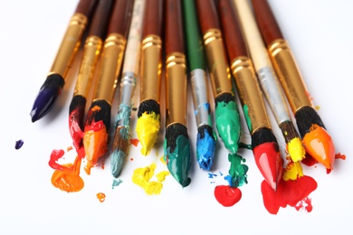 Photo of Brushes with colorful paints on white background, closeup