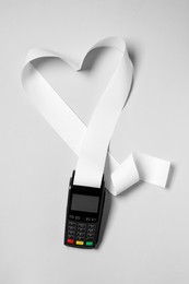 Photo of Payment terminal and heart made of thermal paper for receipt on light grey background, top view