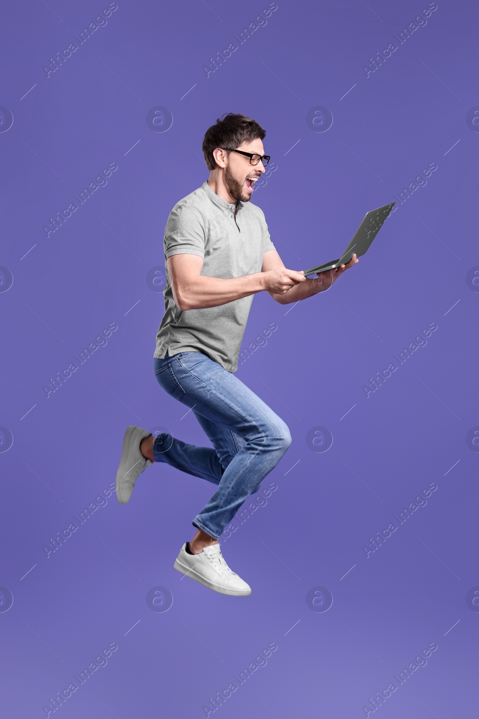 Photo of Happy man with laptop jumping on lilac background