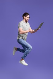 Happy man with laptop jumping on lilac background