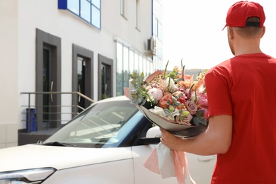 Photo of Delivery man with beautiful flower bouquet near car outdoors, back view