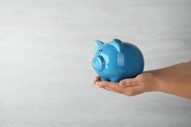 Photo of Woman holding piggy bank on grey background, closeup view. Space for text