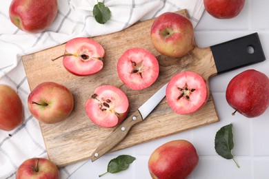 Photo of Tasty apples with red pulp, leaves and knife on white tiled table, flat lay