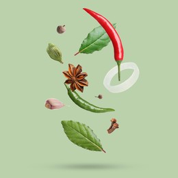 Image of Different spices falling on light green background