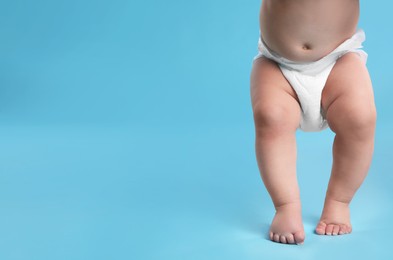 Photo of Cute baby in dry soft diaper standing on light blue background, closeup. Space for text