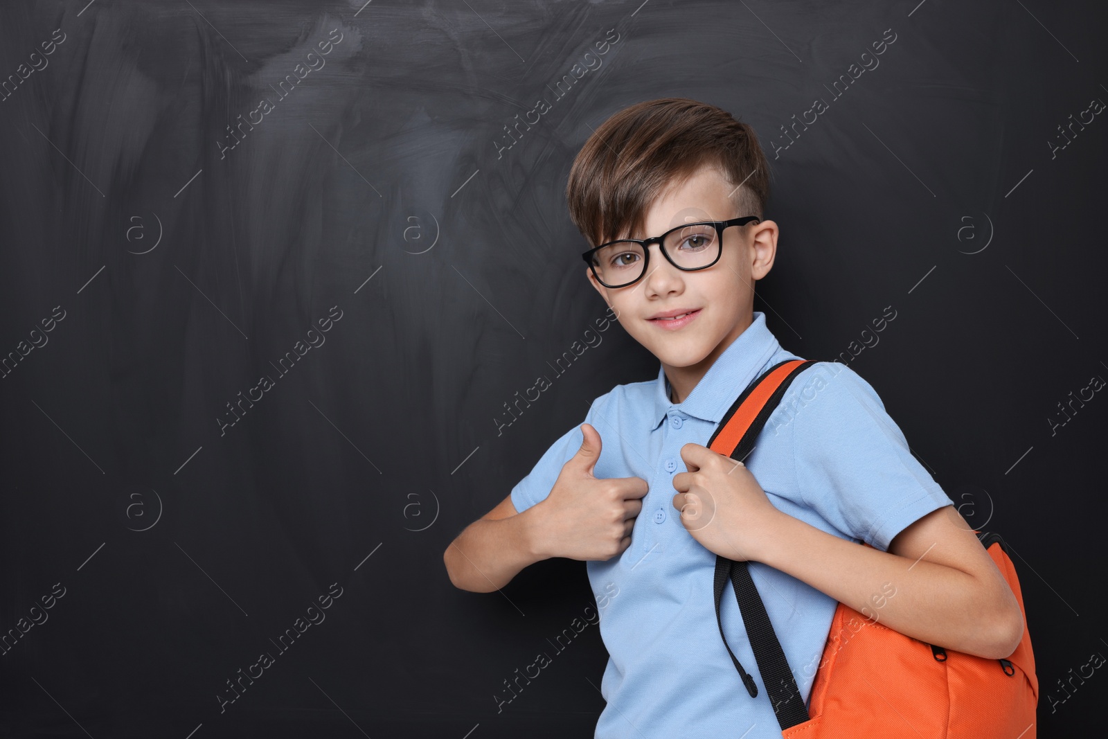 Photo of Cute schoolboy in glasses showing thumbs up near chalkboard, space for text