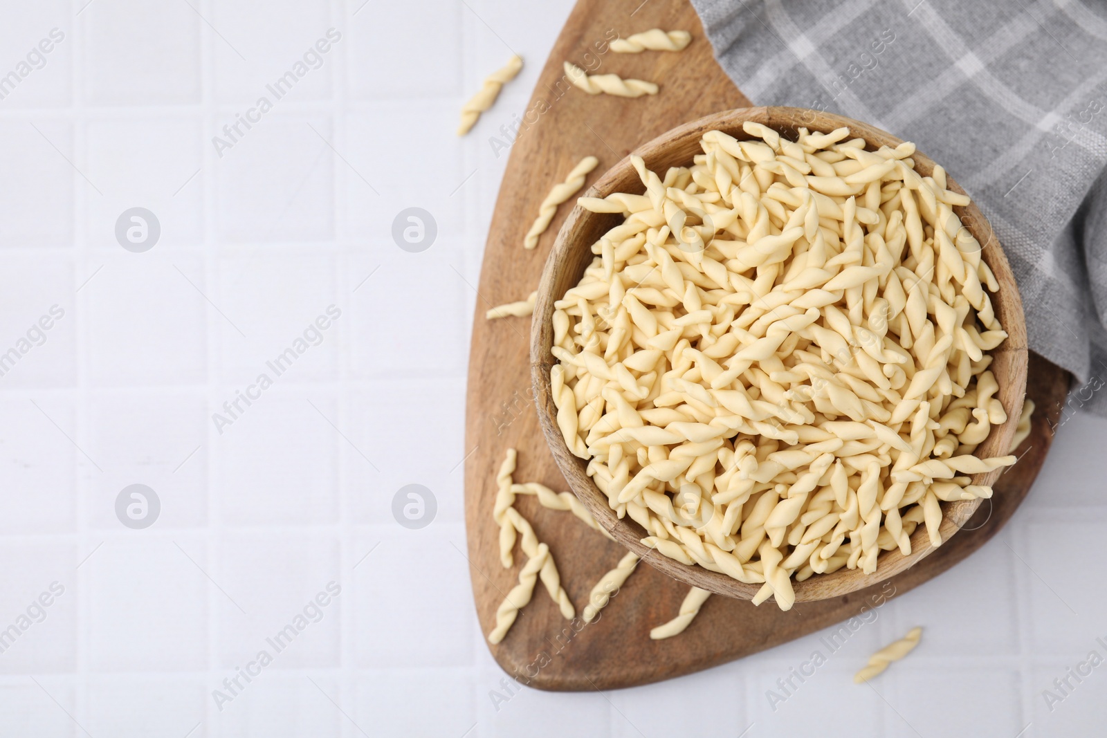 Photo of Bowl with uncooked Italian trofie pasta on white tiled table, flat lay. Space for text