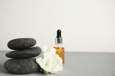 Stack of grey spa stones, flowers and oil on table, space for text